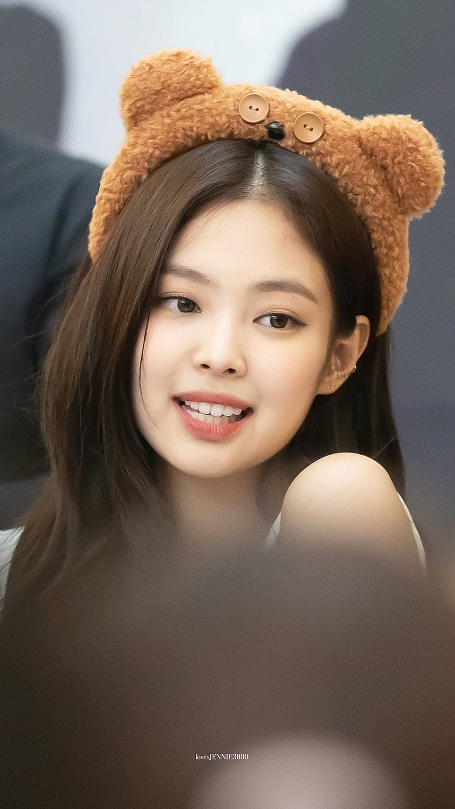 Jennie from Blackpink wearing a cute brown teddy bear headband with button eyes, smiling brightly in a close-up portrait HD phone wallpaper