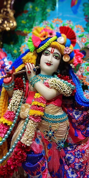 Colorful Krishna Idol Playing Flute With Peacock Feather Crown And Floral Garlands HD phone wallpaper
