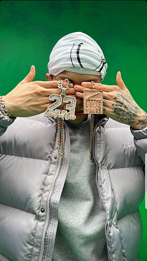 Central Cee wearing a grey puffer jacket and white head wrap holding diamond 23 and Live Yours pendants HD phone wallpaper
