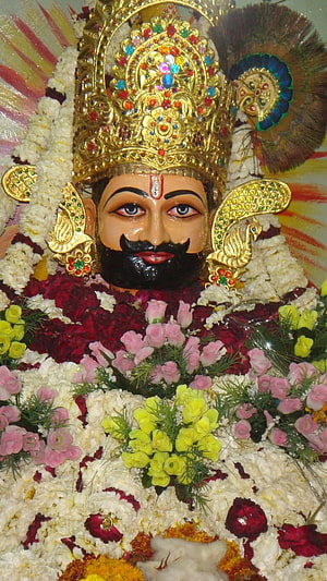 Decorated Statue of Lord Krishna with Peacock Feather Crown and Floral Garlands HD phone wallpaper