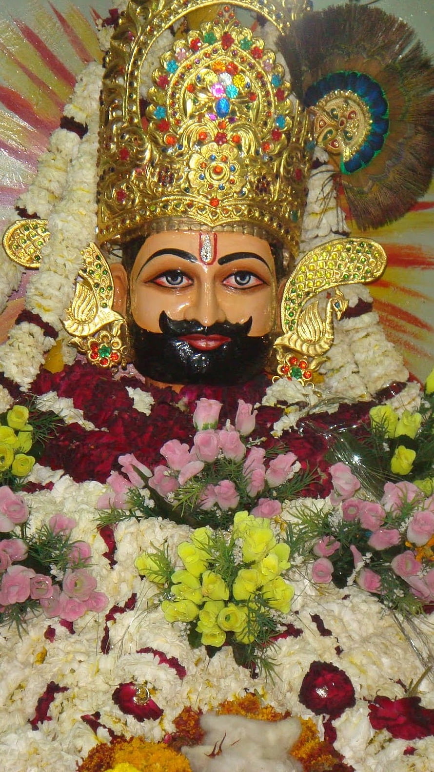 Decorated Statue of Lord Krishna with Peacock Feather Crown and Floral Garlands HD phone wallpaper