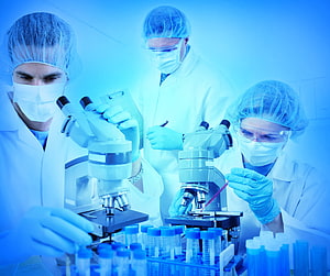 Scientists in protective gear conducting research with microscopes and test tubes in a clinical laboratory HD wallpaper