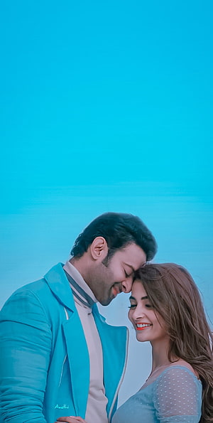 Radhe Shyam and Pooja Hegde in a tender forehead touch against a bright blue sky HD phone wallpaper
