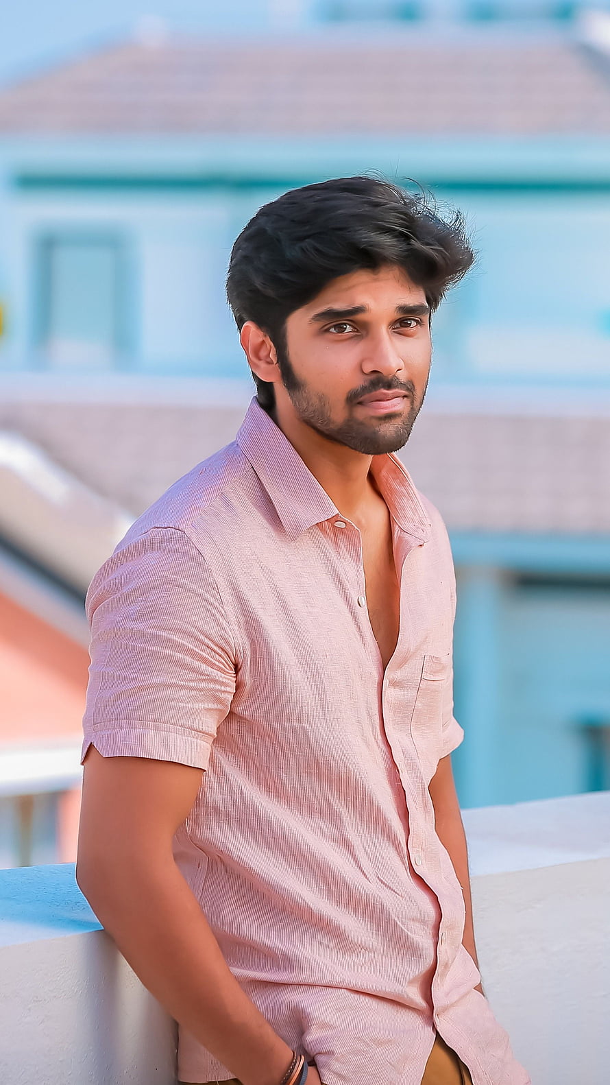 Dhruv Vikram in a light pink short-sleeve shirt leaning on a rooftop ledge HD phone wallpaper