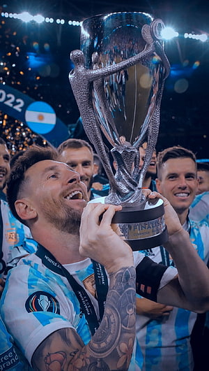 Lionel Messi lifting the Finalissima trophy in his Argentina jersey during a stadium celebration HD phone wallpaper