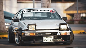 White Toyota Trueno AE86 with widebody kit and pop-up headlights parked on a street HD wallpaper