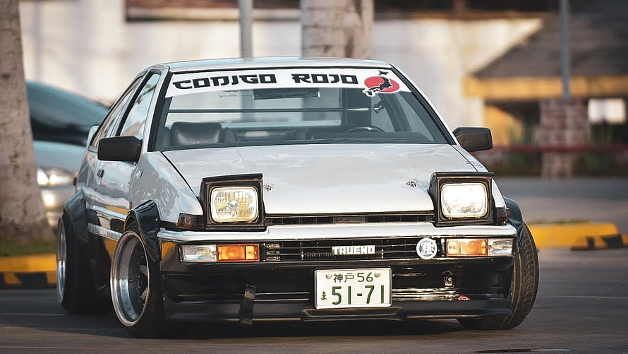 White Toyota Trueno AE86 with widebody kit and pop-up headlights parked on a street HD wallpaper