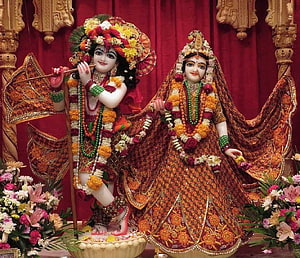 Radha Krishna idols adorned in traditional Indian wedding attire with floral garlands and intricate embroidery HD wallpaper