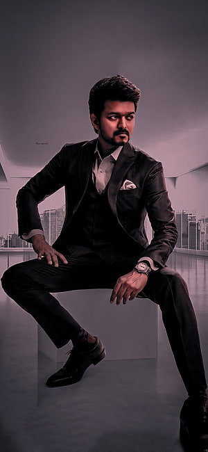 Thalapathy Vijay in a dark three-piece suit seated against a modern city skyline backdrop HD phone wallpaper