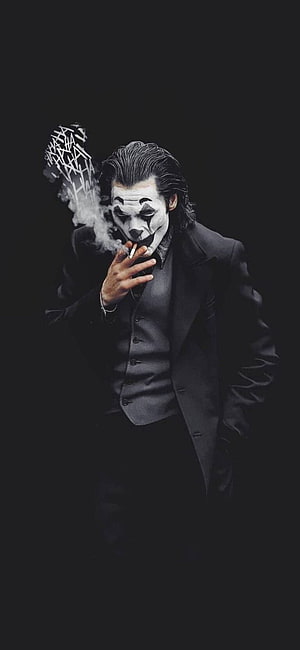 Joker in a black suit smoking a cigarette with dramatic smoke against a dark background HD phone wallpaper