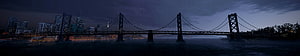 Panoramic Night View of a Suspension Bridge Over a River with a City Skyline in the Background HD wallpaper