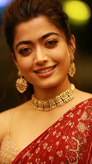 Rashmika Mandanna in a red embroidered saree with gold jewelry and a warm smile HD phone wallpaper