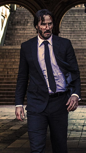 Keanu Reeves as John Wick in a dark suit with blood on his face walking through an archway HD phone wallpaper