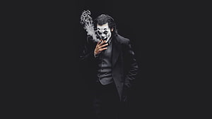 Joaquin Phoenix as the Joker smoking a cigarette in a dark suit against a black background HD wallpaper