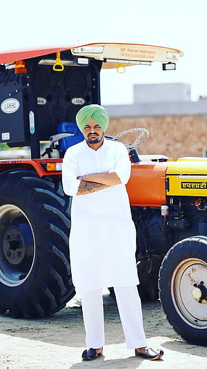 Man in white kurta and green turban standing confidently in front of a customized orange tractor with large speakers, Sidhu Moose Wala, Tractor Background HD phone wallpaper