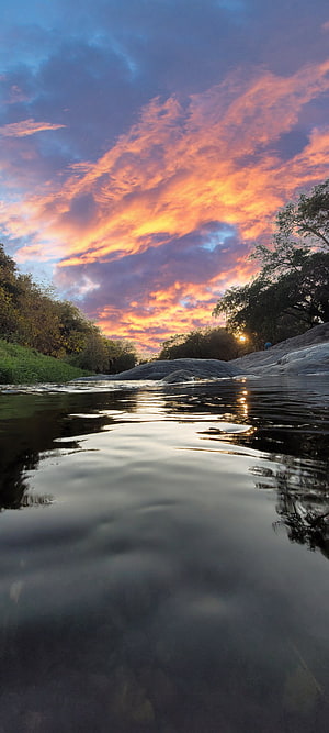 Serene River Sunset with Vibrant Orange Clouds and Calm Water Reflections HD phone wallpaper
