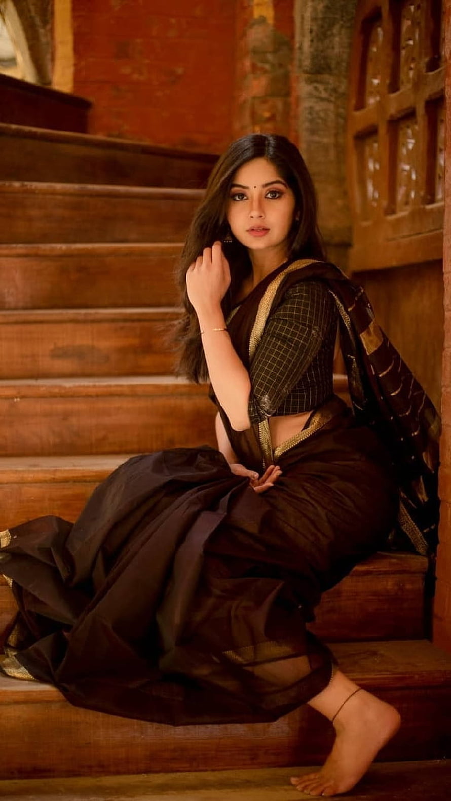 Kashmira Pardeshi in a dark brown saree seated on rustic wooden stairs HD phone wallpaper