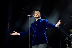 Atif Aslam performing on stage in a blue velvet jacket with arms outstretched HD wallpaper