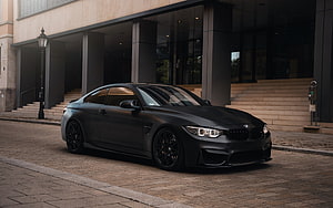 Matte Black BMW M4 Coupe Parked on Cobblestone Street in Front of Modern Building HD wallpaper