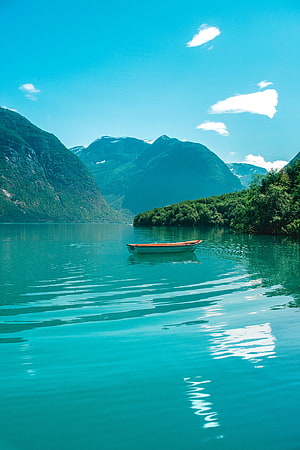 Serene turquoise fjord with a lone wooden boat floating on calm waters surrounded by lush green mountains HD phone wallpaper