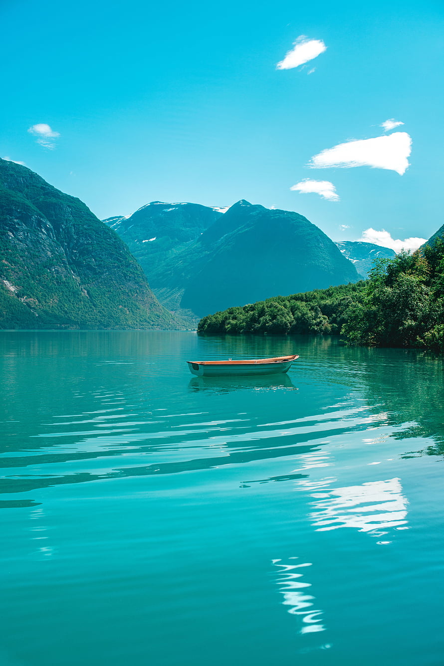 Serene turquoise fjord with a lone wooden boat floating on calm waters surrounded by lush green mountains HD phone wallpaper