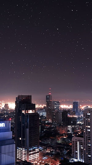 Starry Night Sky Over Illuminated City Skyline with Glowing High-Rise Buildings HD phone wallpaper