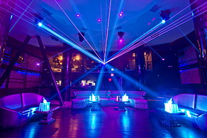 Vibrant nightclub lounge with sweeping blue and purple laser beams and modern seating HD wallpaper