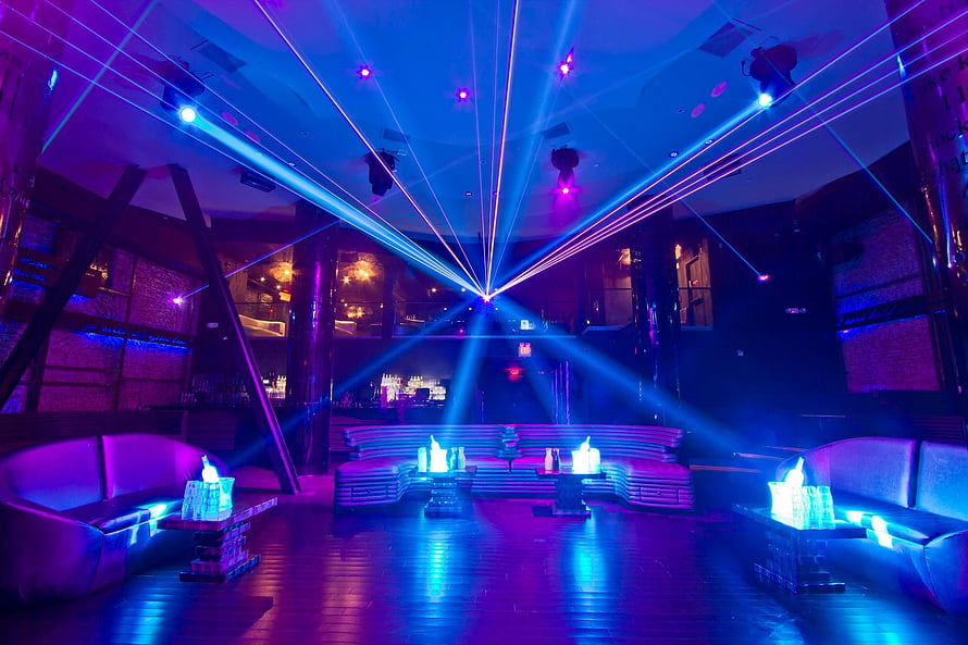 Vibrant nightclub lounge with sweeping blue and purple laser beams and modern seating HD wallpaper