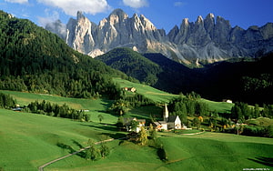 Alpine Village with Church and Farmhouses in Green Pastures Beneath Dramatic Dolomite Peaks HD wallpaper