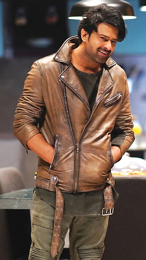 Prabhas in a rugged brown leather jacket and olive cargo pants with a confident smile HD phone wallpaper