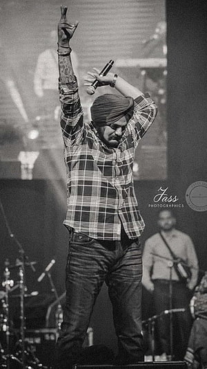 Diljit Dosanjh performing live on stage in a plaid shirt and turban, black and white concert photography HD phone wallpaper