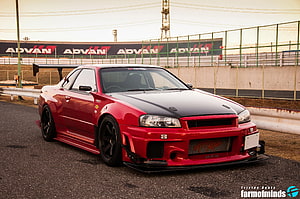 Red Nissan Skyline GT-R R34 Widebody at a Race Track with ADVAN Banners HD wallpaper