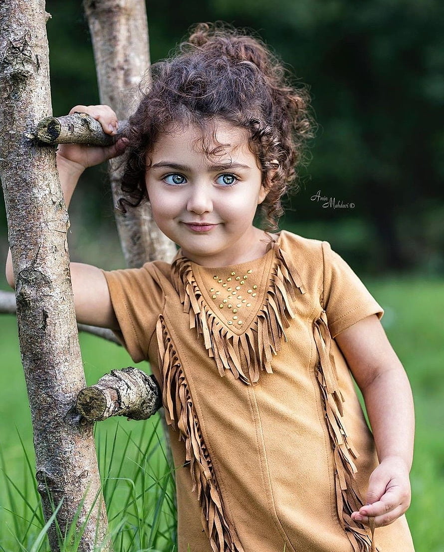 Young Girl in Fringed Tan Dress Leaning on Tree Branch in Green Meadow HD phone wallpaper