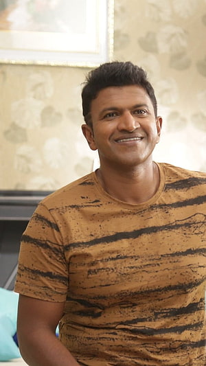 Puneeth Rajkumar smiling portrait in a tiger-striped t-shirt HD phone wallpaper