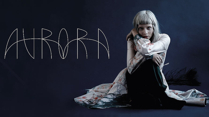 Aurora Aksnes in a floral robe seated against a dark studio backdrop HD wallpaper