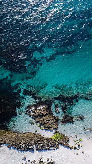 Aerial View of Turquoise Ocean Water Over Rocky Coastline and White Sand Beach HD phone wallpaper