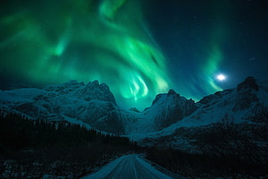 Vivid Green Aurora Borealis Dancing Over Snow-Capped Mountain Peaks and a Winding Winter Road HD wallpaper