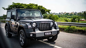 Black Mahindra Thar SUV on a Scenic Highway with Lush Green Foliage and Distant Cityscape HD wallpaper