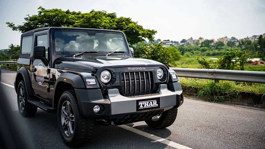 Black Mahindra Thar SUV on a Scenic Highway with Lush Green Foliage and Distant Cityscape HD wallpaper