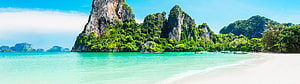 Tropical limestone karst islands rising from turquoise sea with white sand beach and longtail boats HD wallpaper