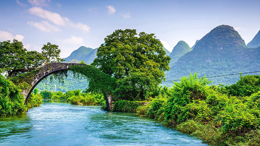 Scenic stone arch bridge over a river with lush green karst mountains in the background HD wallpaper