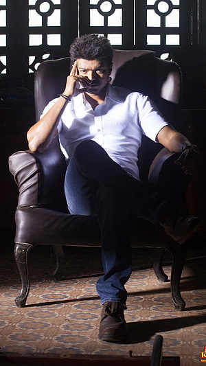 Vijay Sethupathi sitting in a leather chair wearing a white shirt and jeans in a dimly lit room HD phone wallpaper