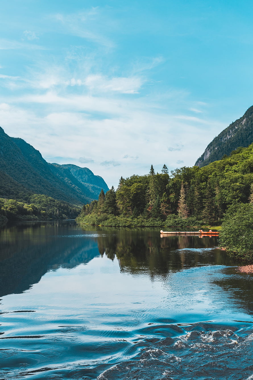 Serene Mountain Lake with Canoe and Forested Shoreline Under Blue Sky HD phone wallpaper