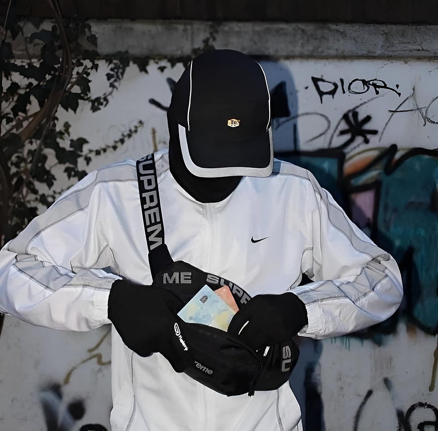 Anonymous figure in white Nike jacket and black cap holding cash against graffiti wall HD wallpaper