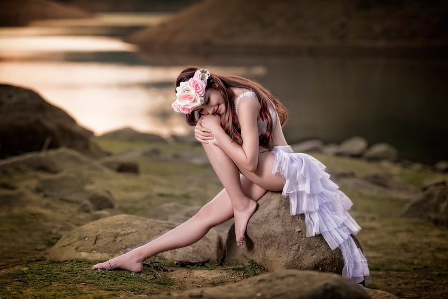 Woman in white ruffled dress and floral headpiece sitting on a rock by a lake at sunset, Asian Beauty, asian, beautiful, girl, legs, wreath HD wallpaper