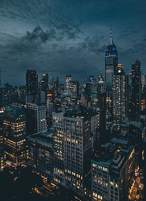 Empire State Building Illuminated in Blue Against a Dramatic Cloudy Night Sky in New York City HD phone wallpaper