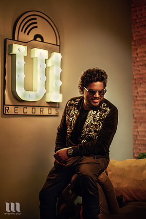 Yuvan Shankar Raja in a gold-embroidered jacket and sunglasses seated beside a U1 Records marquee sign HD phone wallpaper