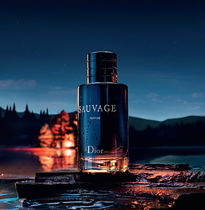Dior Sauvage Parfum Bottle on Wet Rocks at Night with Campfire Glow and Starry Sky HD phone wallpaper