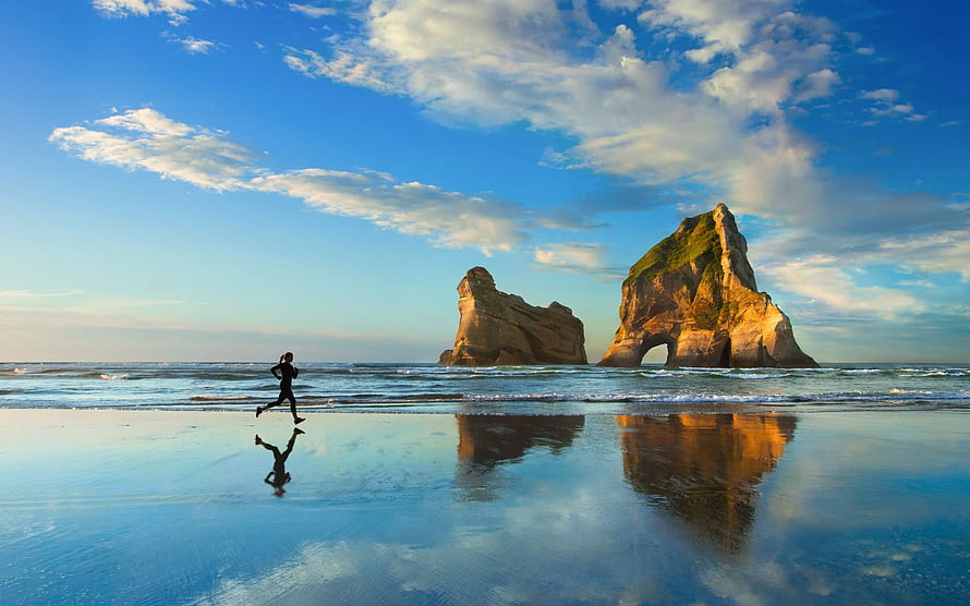 Runner Silhouette on Wet Sand at Wharariki Beach with Rock Formations HD wallpaper