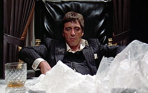 Tony Montana in a pinstripe suit reclining in a black leather chair with a glass of whiskey HD wallpaper